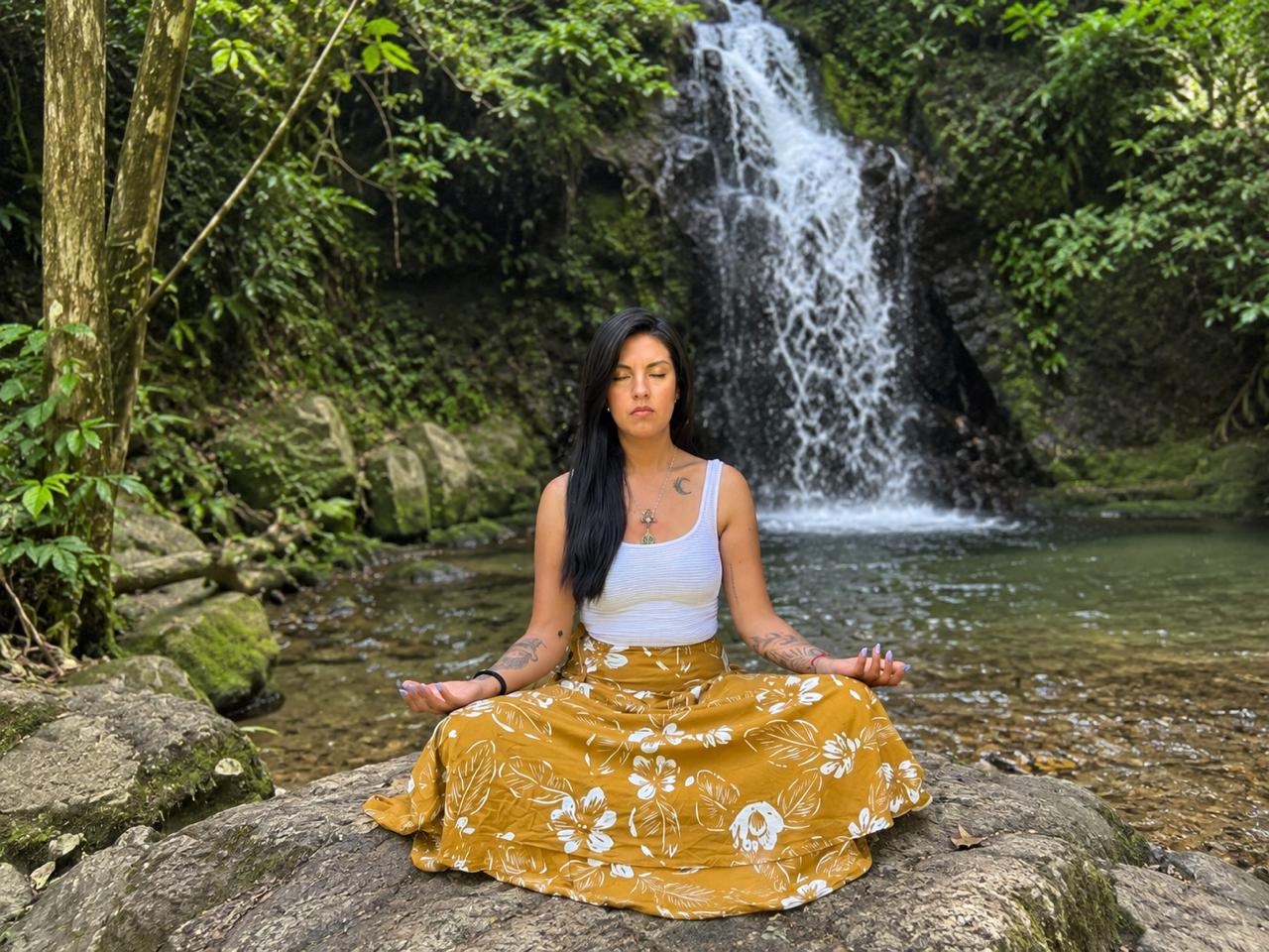 María Arellano meditando frente a una cascada rodeada de naturaleza